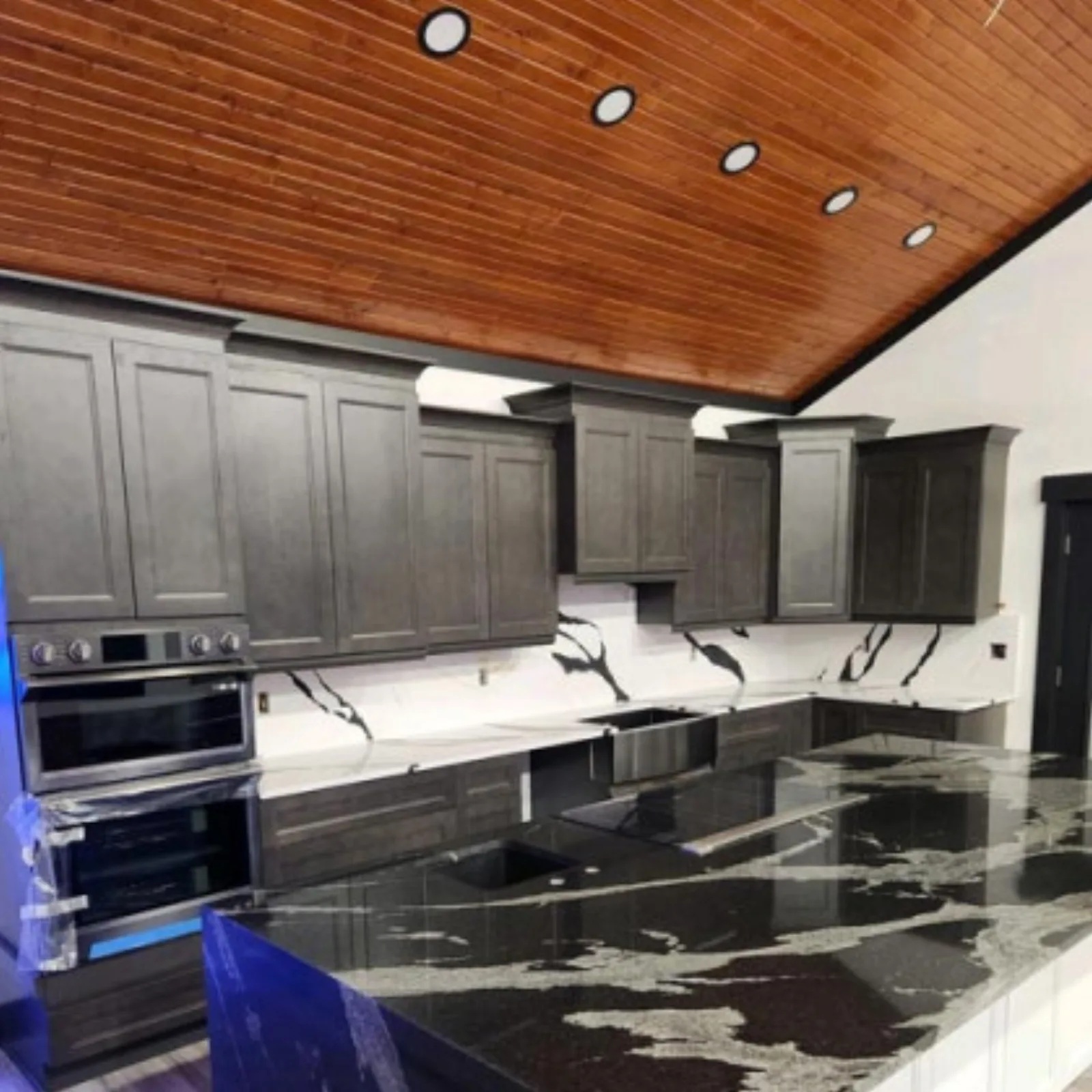 Grey kitchen with black marble counters under a wood plank ceiling