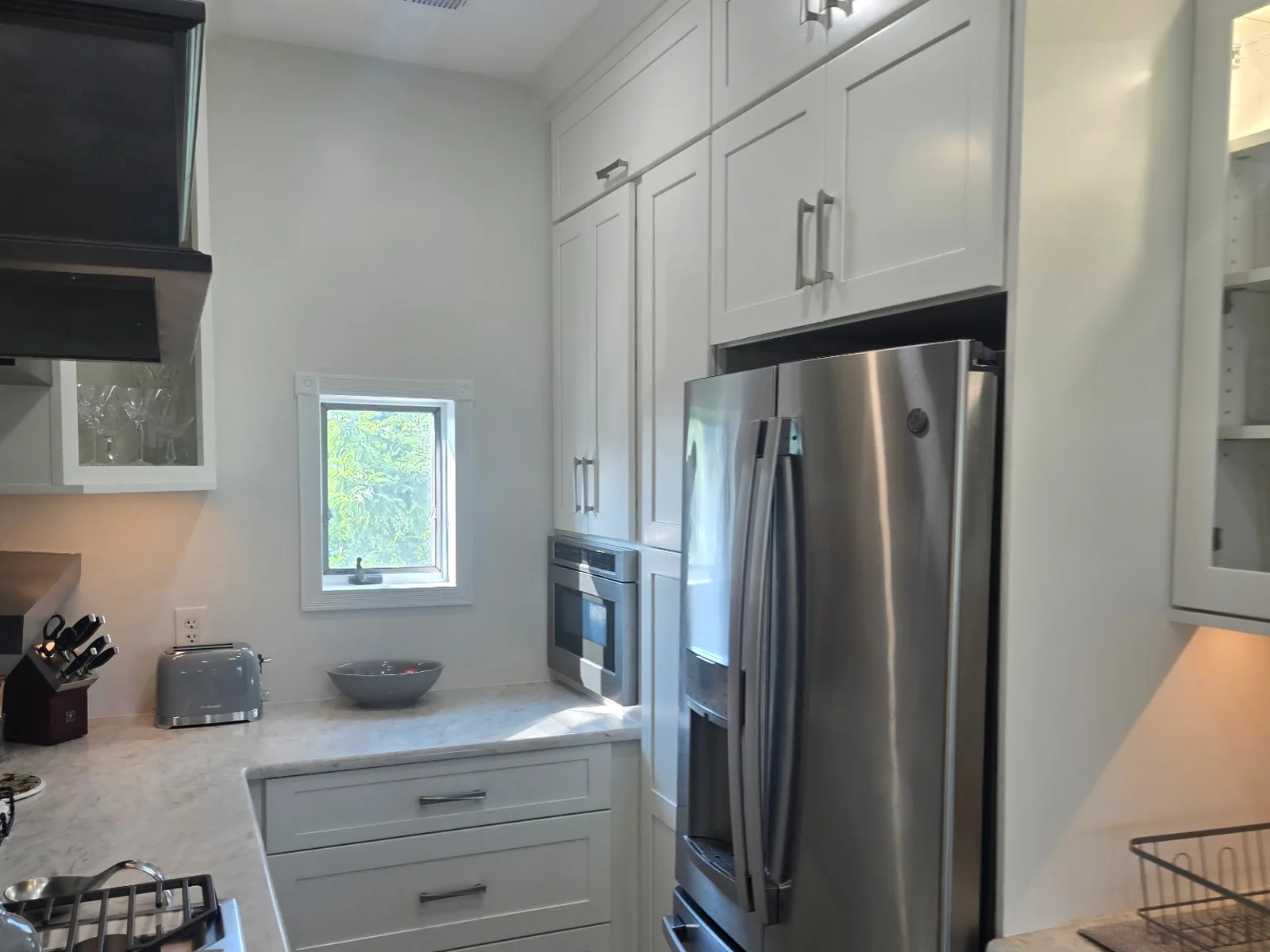 Kitchen corner with tall cabinetry, a wall oven and a window above the counter run
