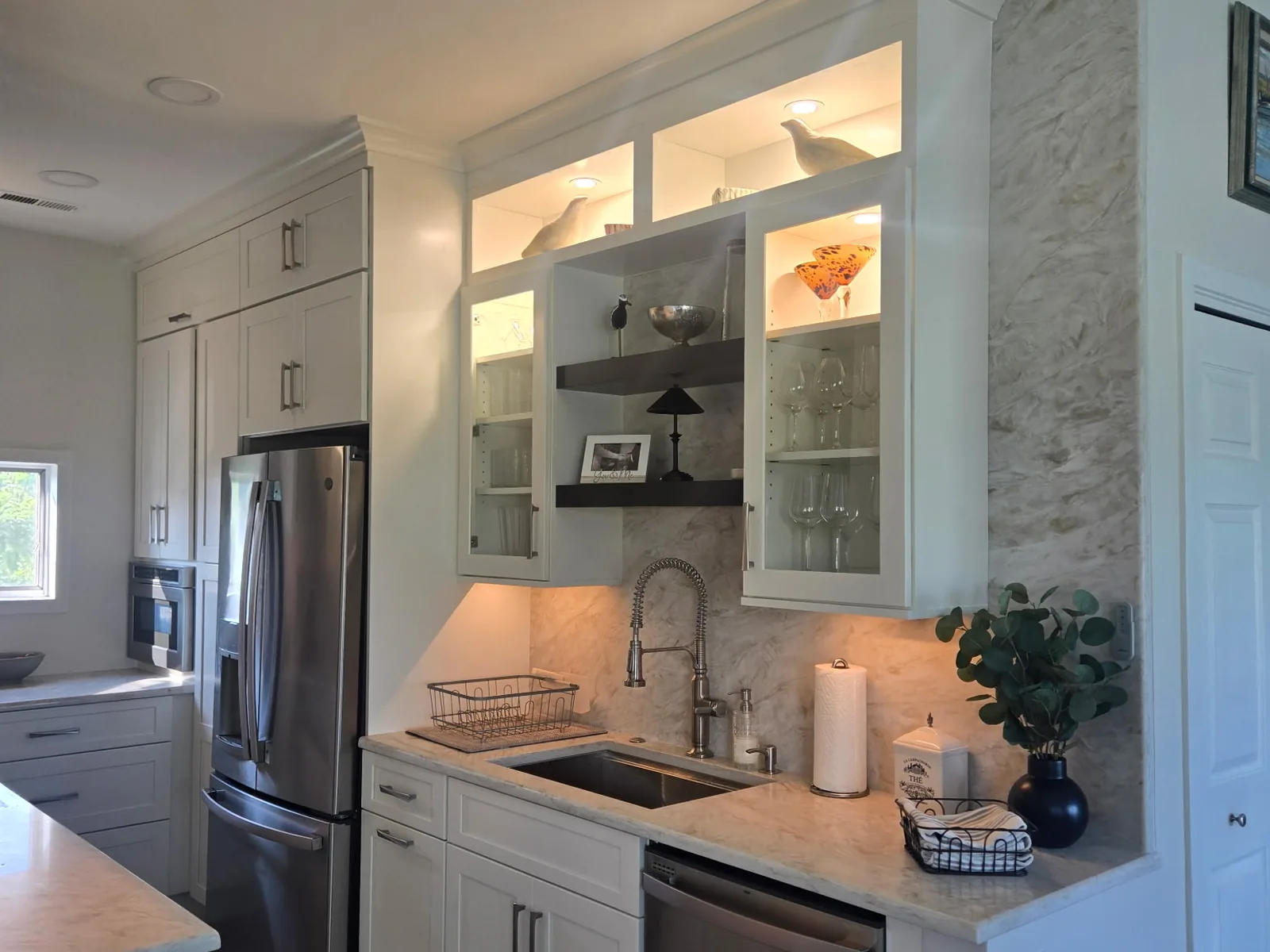 Kitchen prep run with lit glass front cabinets, an undermount sink and a stone clad column