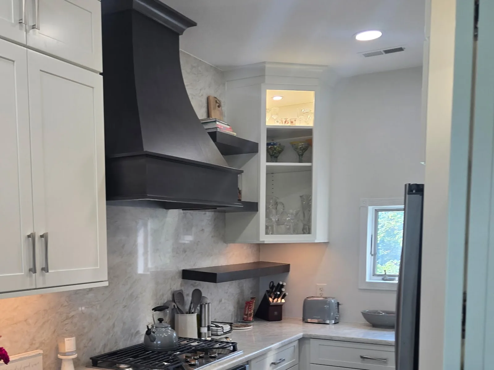 Kitchen range wall with a dark hood surround, floating shelf and a corner counter run beyond