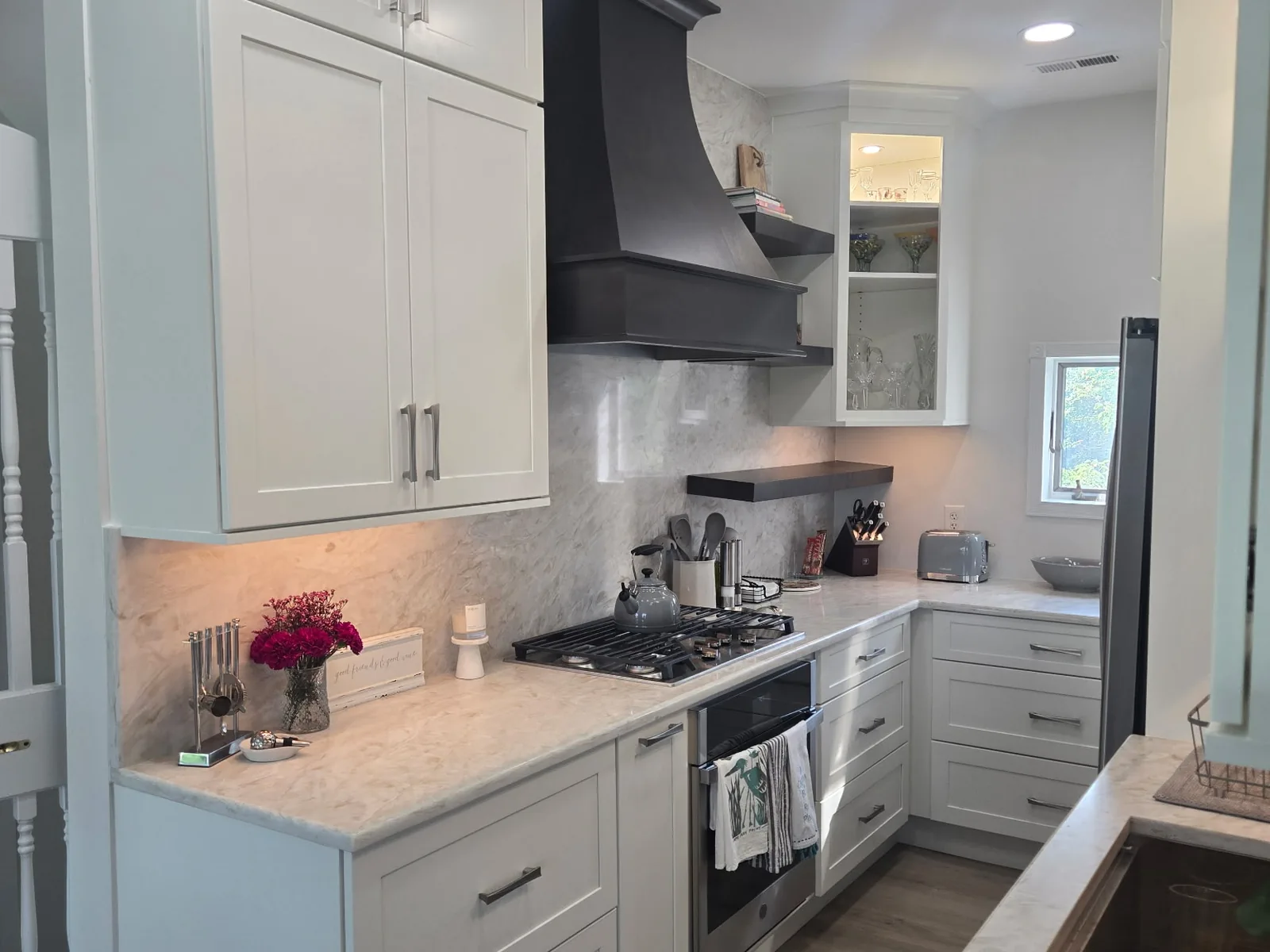 White shaker kitchen with a full height stone backsplash and a dark curved range hood