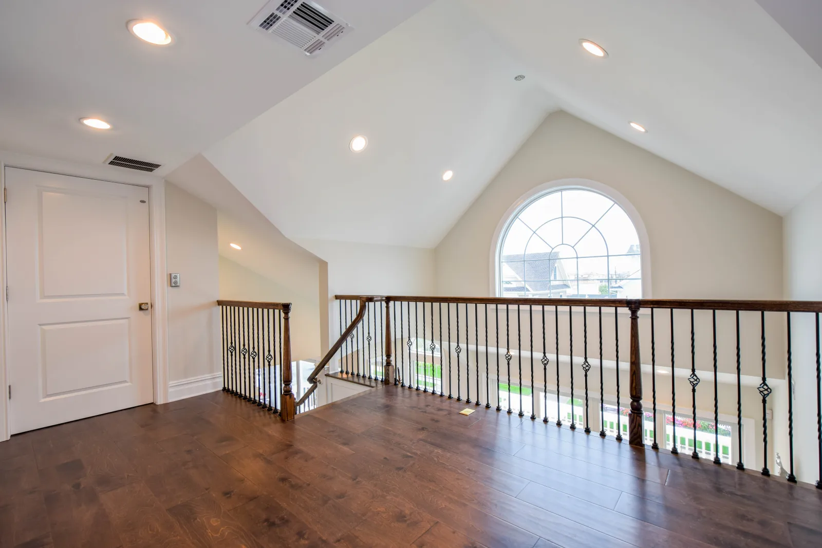 Second floor landing with wood floors and an arched window